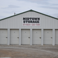 Midtown Storage building with five white roller doors and a sign displaying the name and two phone numbers.