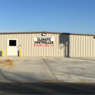 Exterior view of a beige metal storage building with a single door and a climate-controlled signage sign.