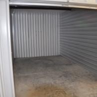An empty storage unit with gray corrugated metal walls and a concrete floor, seen from the open doorway.