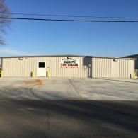 A beige, metal-sided commercial building with a single white door and a sign for 