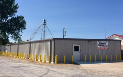 A single-story, gray metal storage building with yellow bollards and a sign reading 