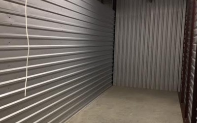 An empty storage unit with corrugated metal walls and a concrete floor.