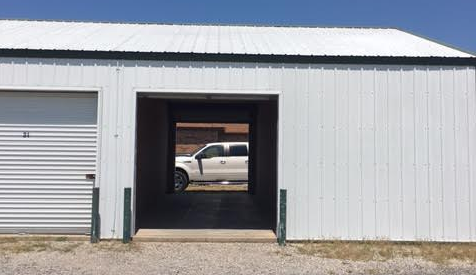A white storage building with a closed roll-up door and an open bay revealing a white pickup truck parked behind it.