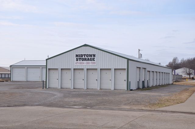 A white Midtown Storage building with multiple roll-up garage doors on a paved lot under a cloudy sky.