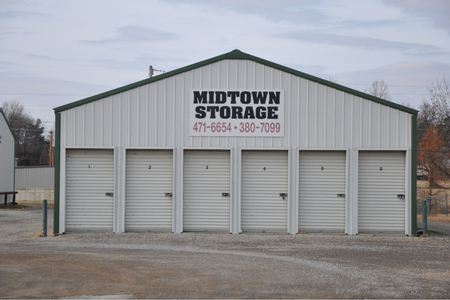 A gray, metal Midtown Storage building featuring six white, numbered roll-up garage doors and two phone numbers.