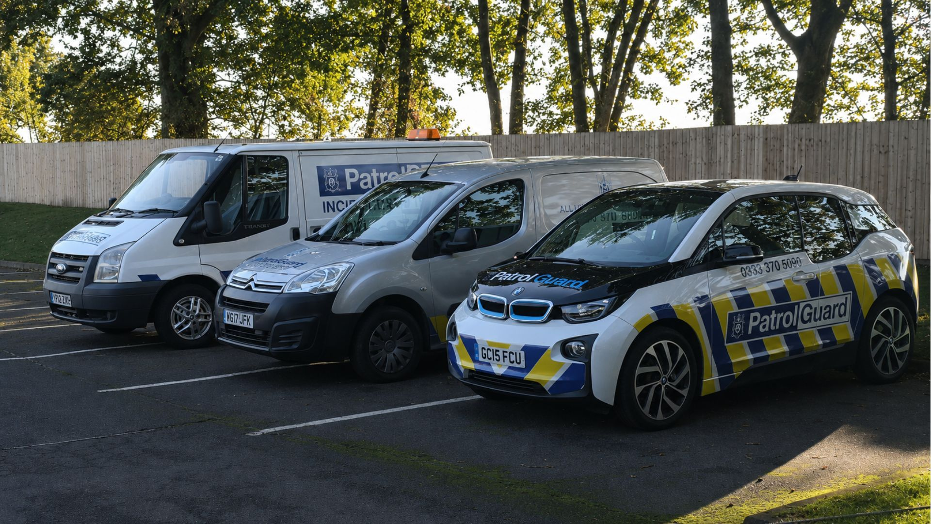 Three PatrolGuard branded vehicles parked in a car park surrounded by trees; one car, one small van