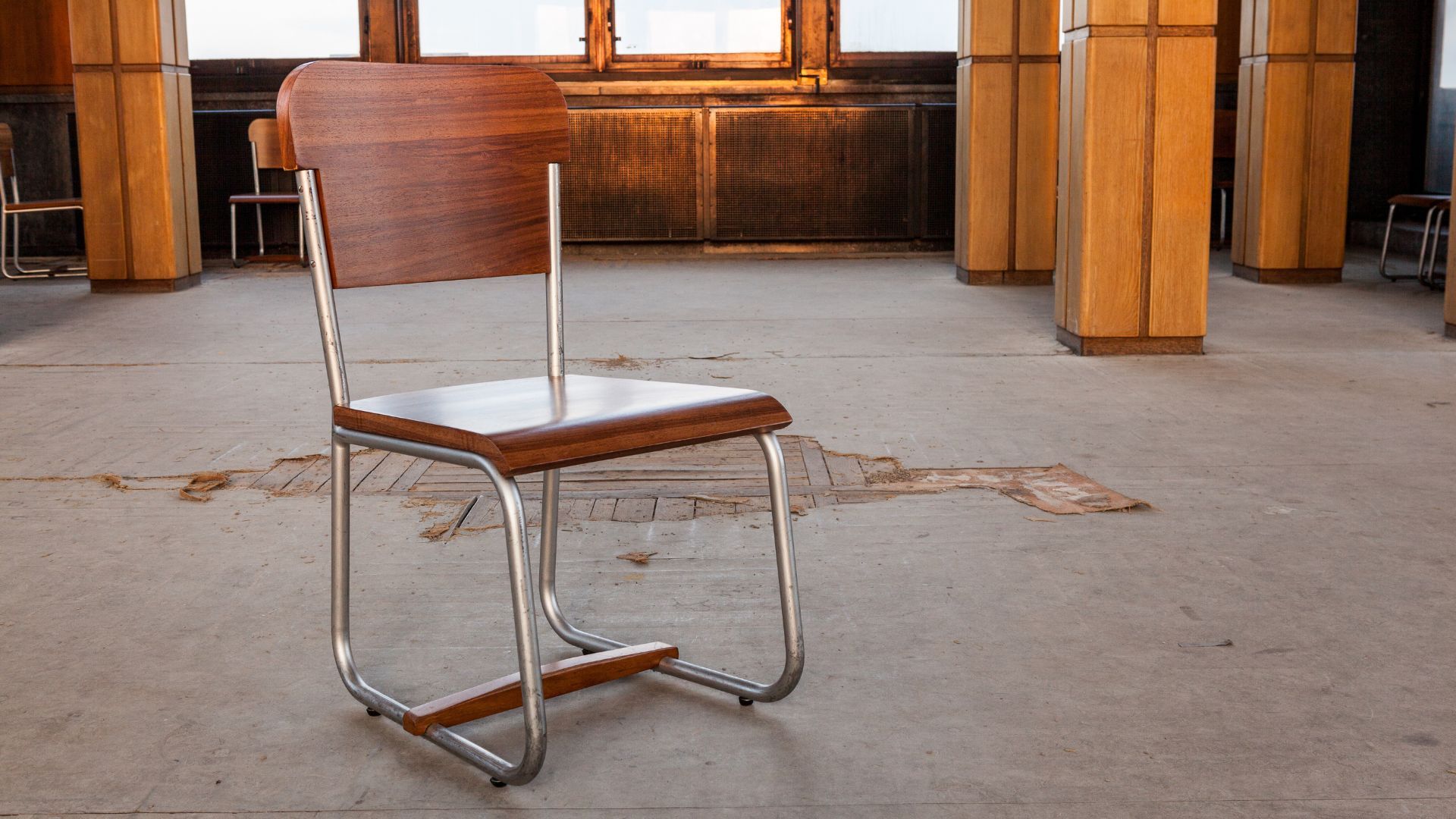 A wooden chair with a metal frame sitting in the middle of a disused building. 