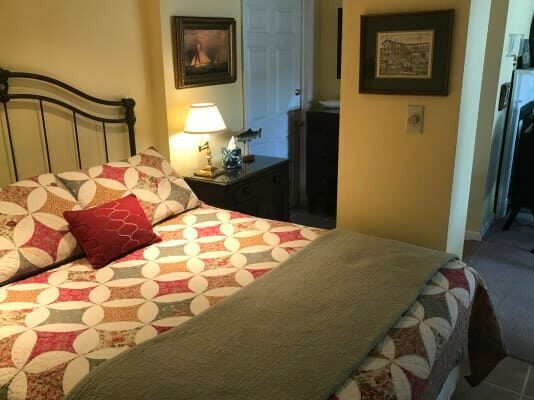 A bedroom with a bed , nightstand , lamp and picture on the wall.