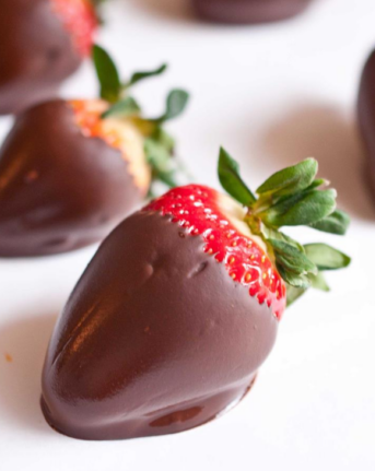 A close up of a chocolate covered strawberry on a white surface