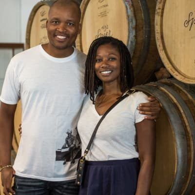 A man and a woman are posing for a picture in front of wine barrels.