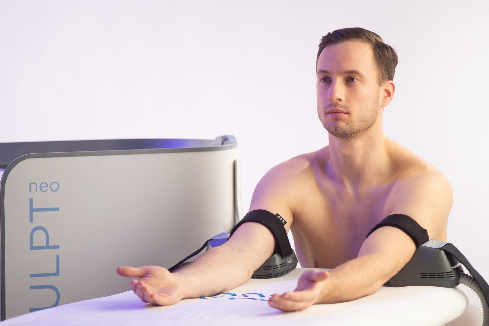 A shirtless man is sitting on a surfboard with his arms outstretched.