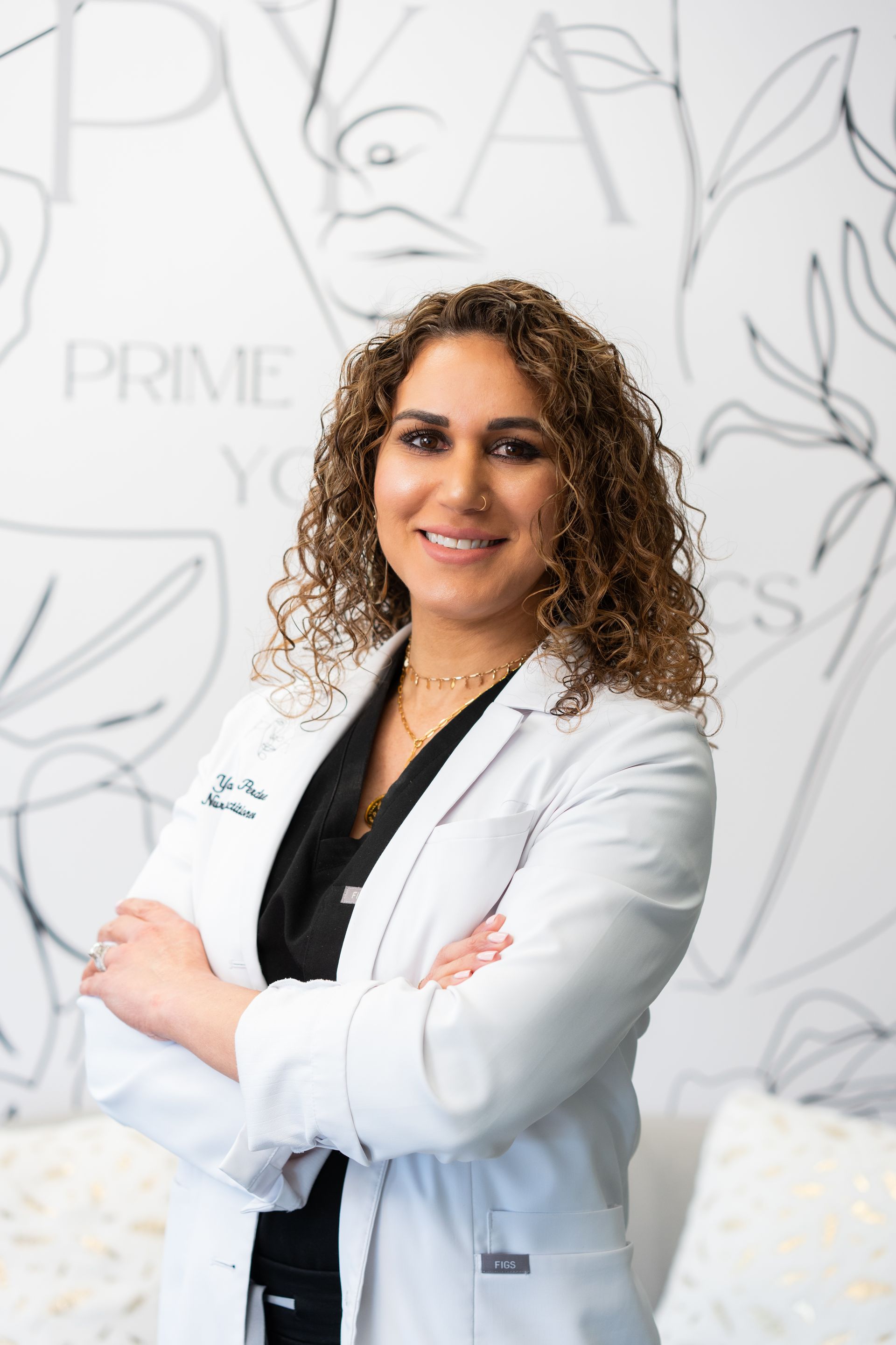 A woman with curly hair is wearing a white lab coat and a black shirt.