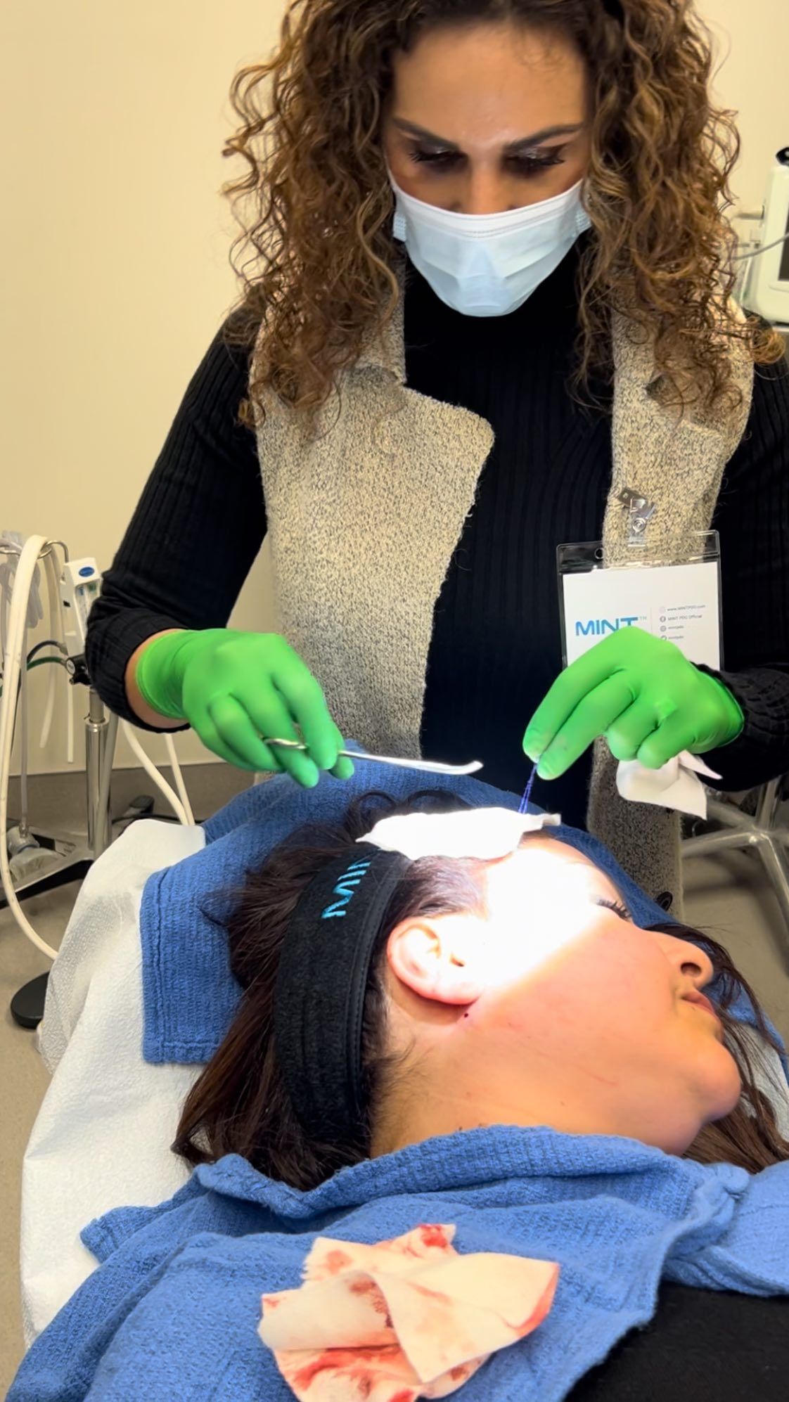 A woman wearing a mask and green gloves is cleaning a woman 's face.