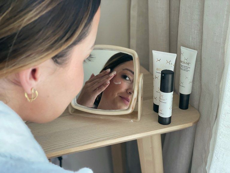 A woman is looking at her face in a mirror.