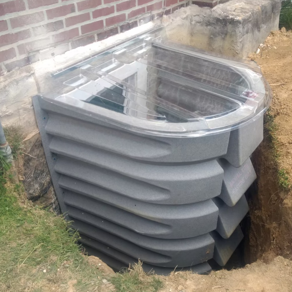 A window well in the ground next to a brick wall.