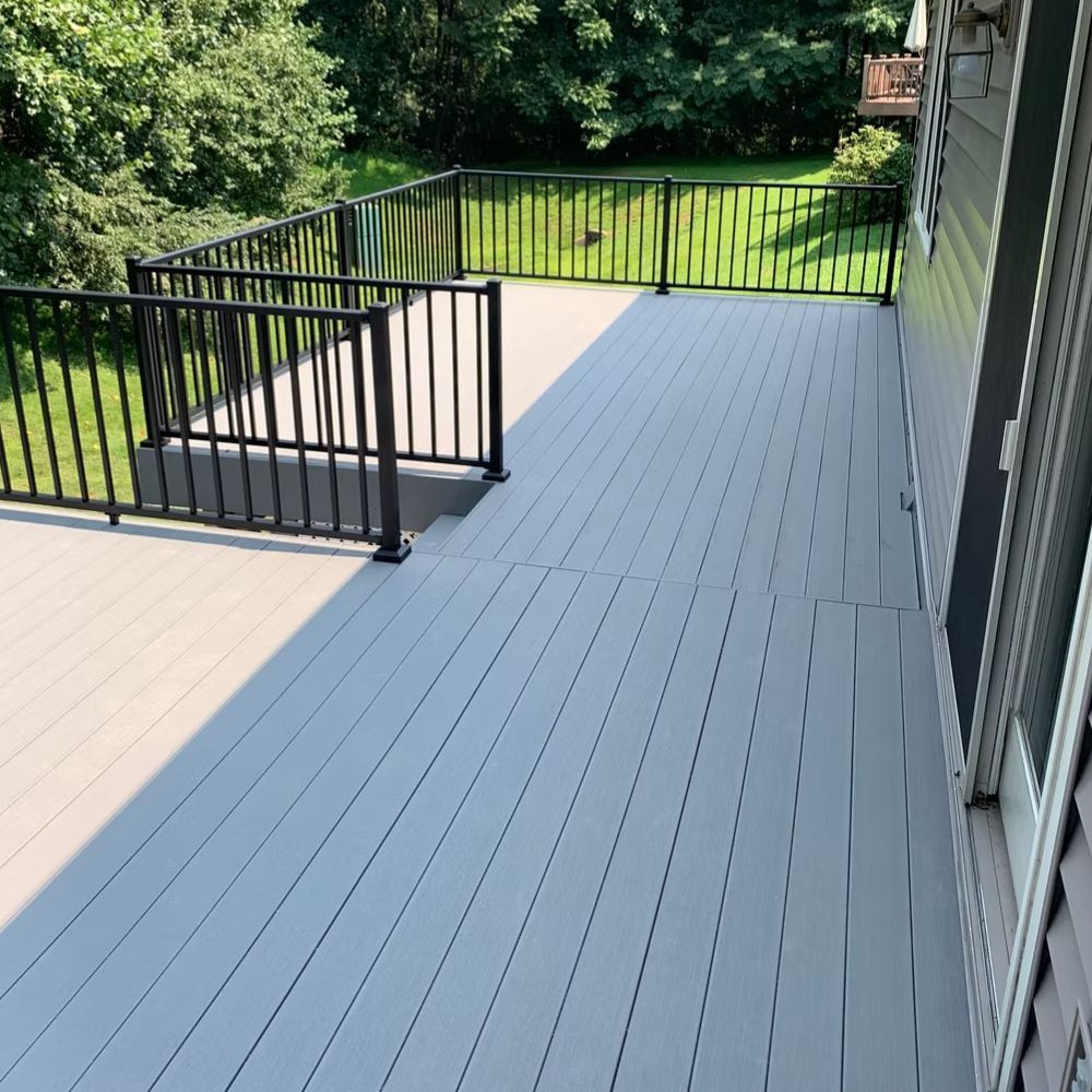 A gray deck with a black railing and trees in the background