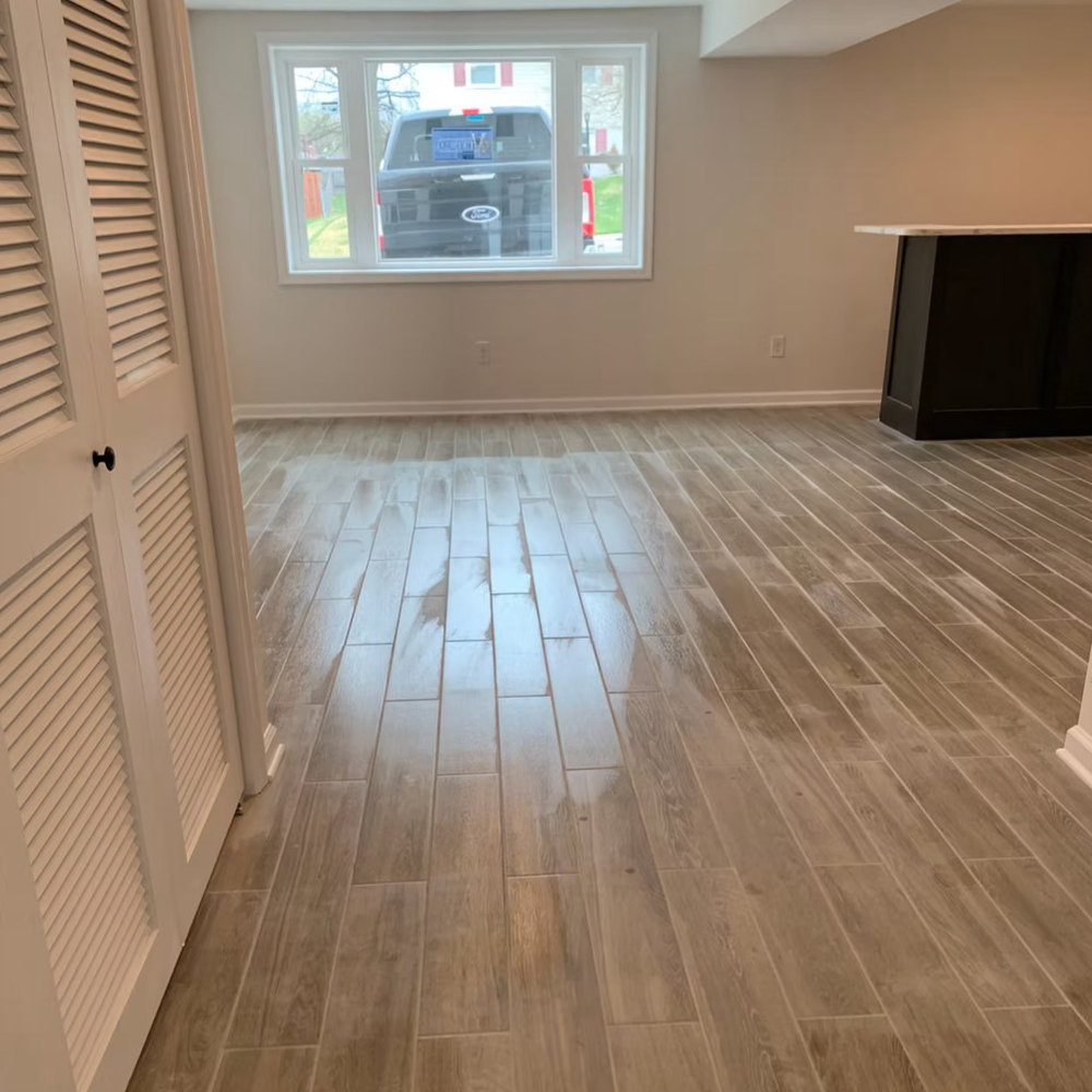 An empty room with wood-look tile floor and white shutters, a small bar, and window with car visible.