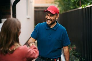 Two people shaking hands outdoors, smiling near a house and black fence.