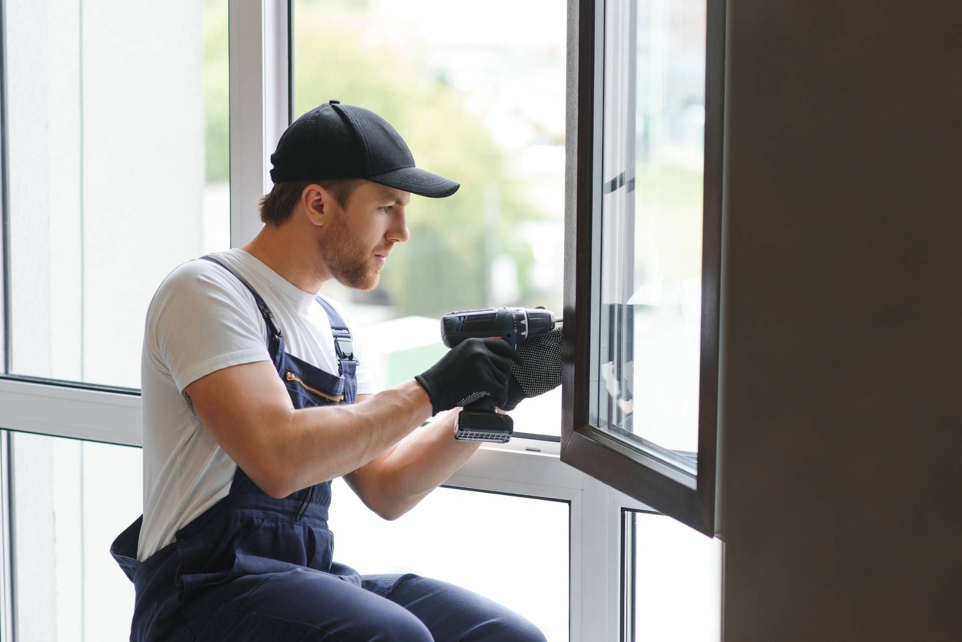 Worker in black cap and gloves installing a window indoors