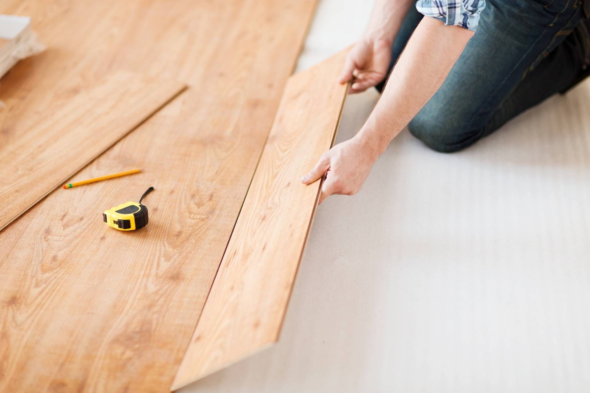 Person installing light wood laminate flooring with a tape measure and pencil nearby