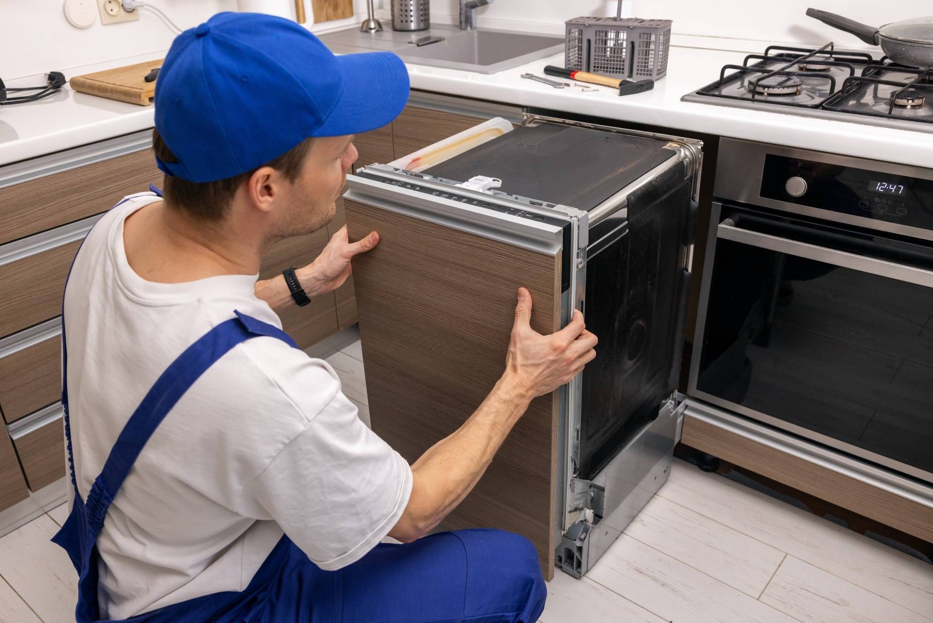 Technician sliding a built-in oven into a kitchen cabinet, with a second oven nearby