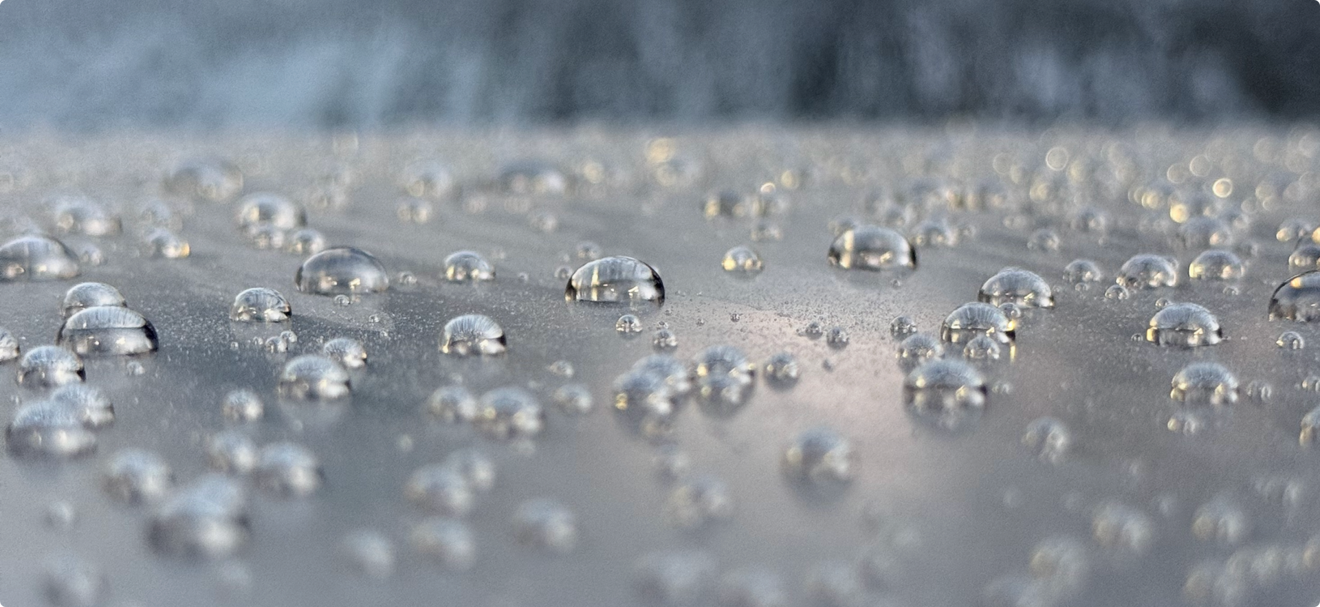 Clear water droplets scattered across a smooth, matte gray surface.