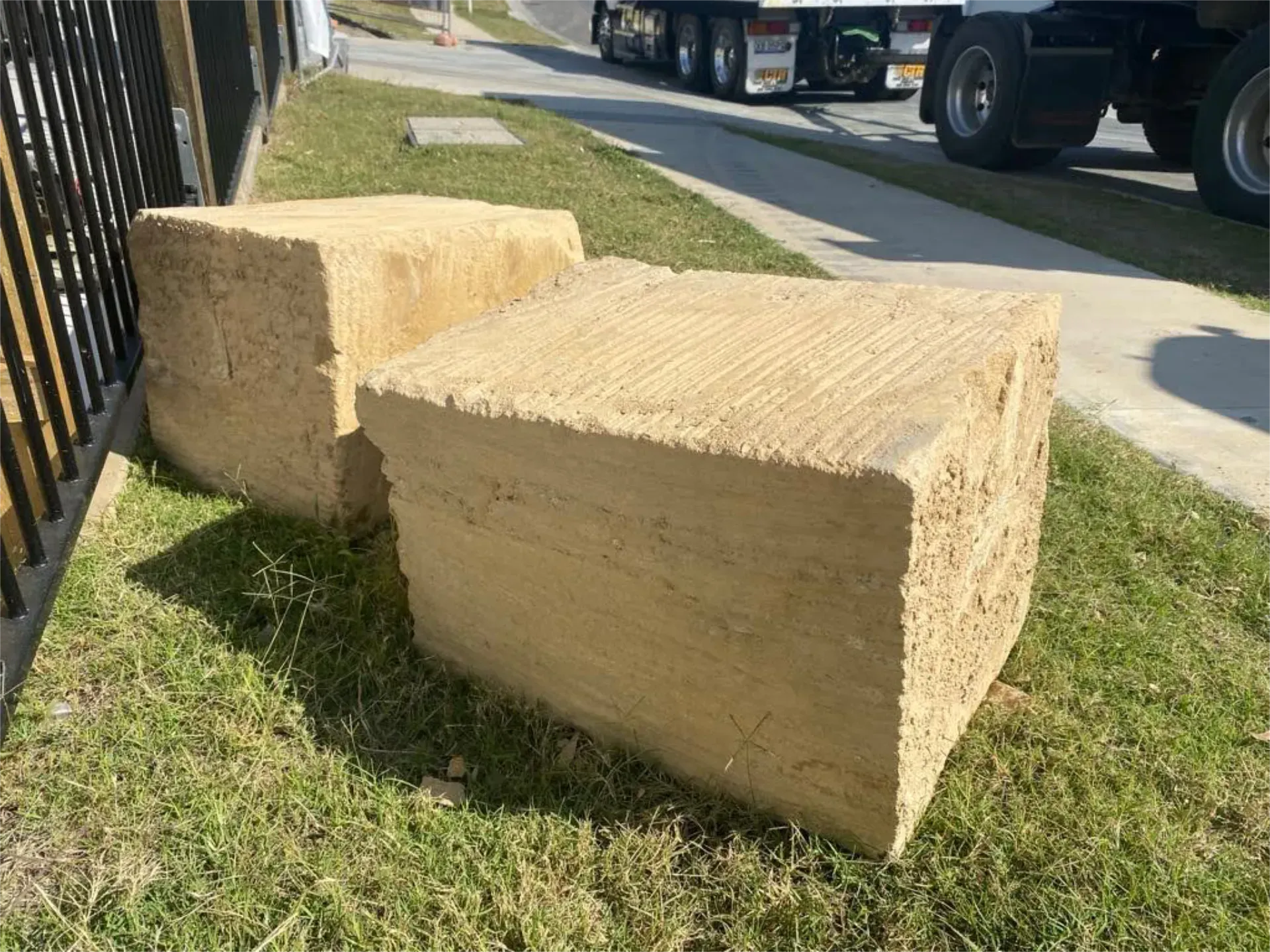 Two large blocks of sandstone are sitting in the grass next to a truck.
