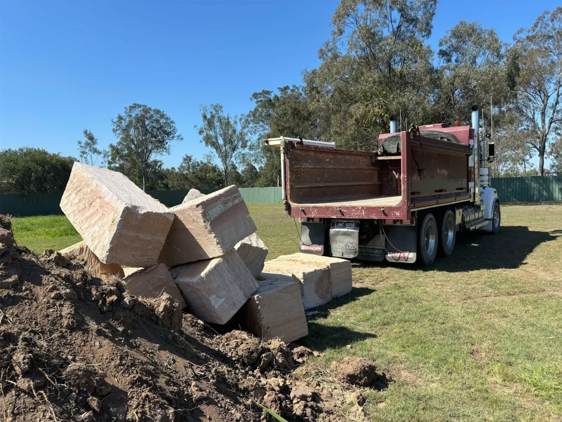 A dump truck is carrying a pile of sandstone rocks in a field.