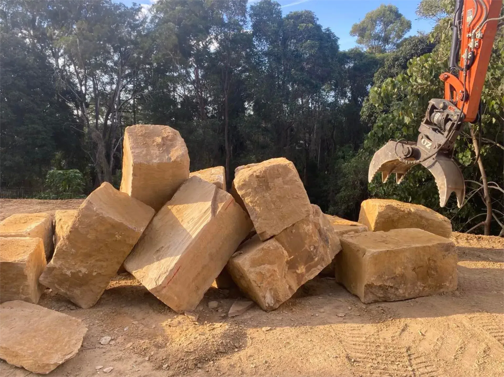 A pile of sandstone rocks is being lifted by an excavator.