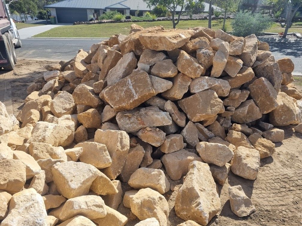 A pile of sandstone rocks is sitting in the dirt in front of a house.