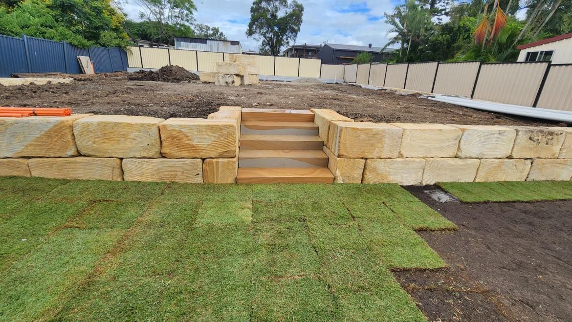 A sandstone wall with stairs leading up to it is sitting on top of a lush green field.