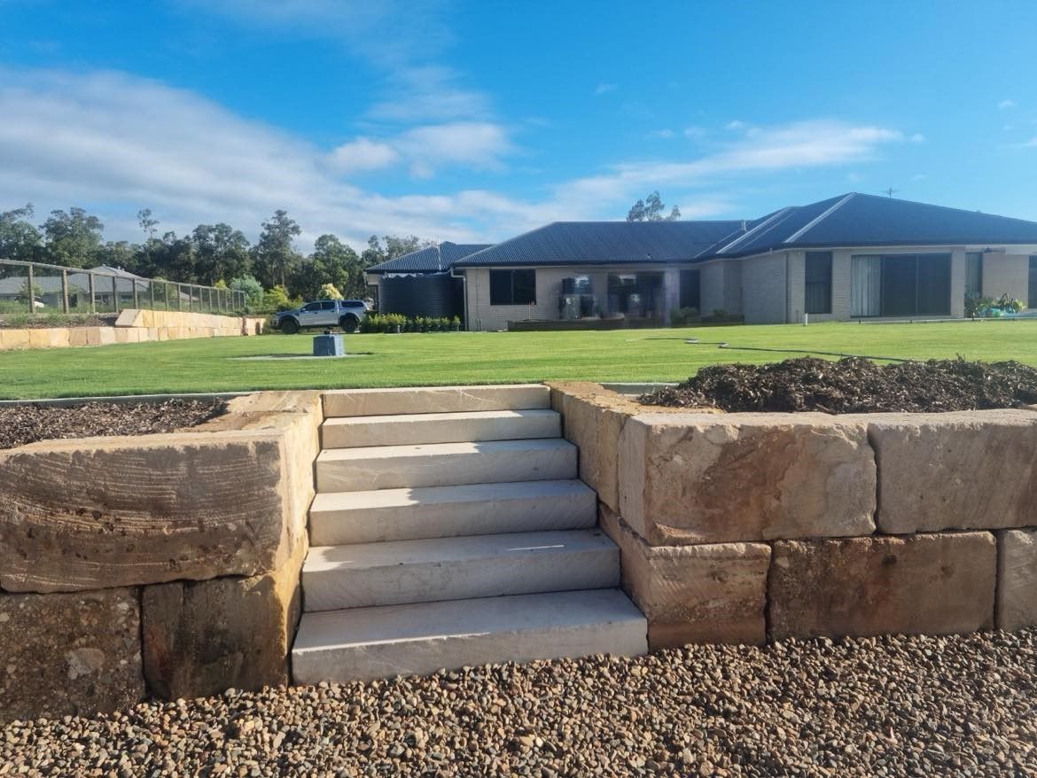 A house is behind a sandstone wall with stairs leading up to it.