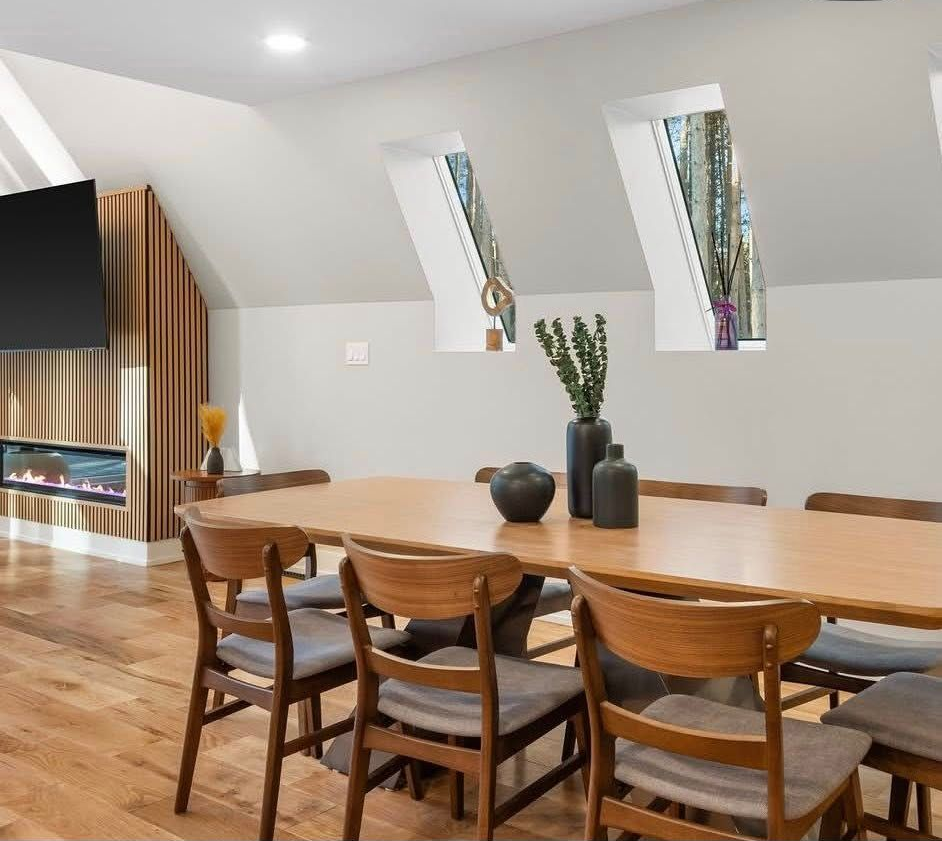 Modern dining room with long wooden table, chairs, and slanted skylight windows.