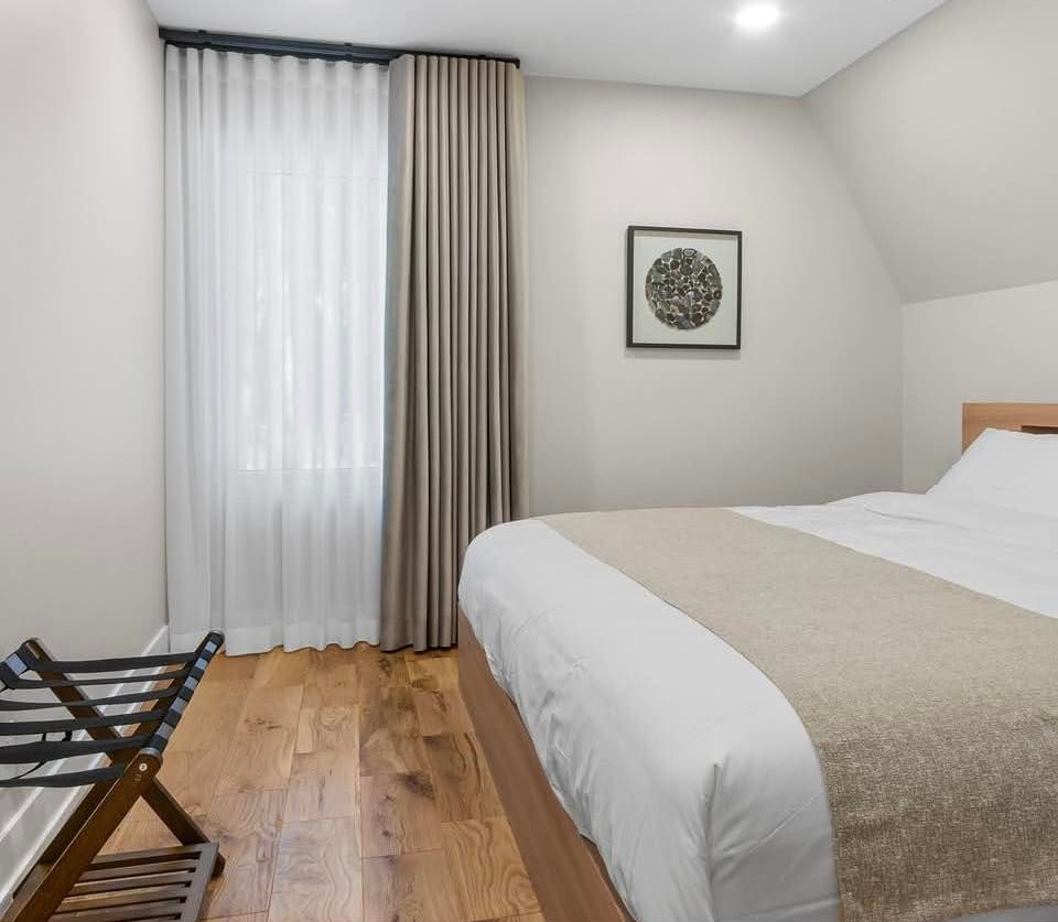 Minimal bedroom with a bed, white curtains, wooden floor, and framed wall art.