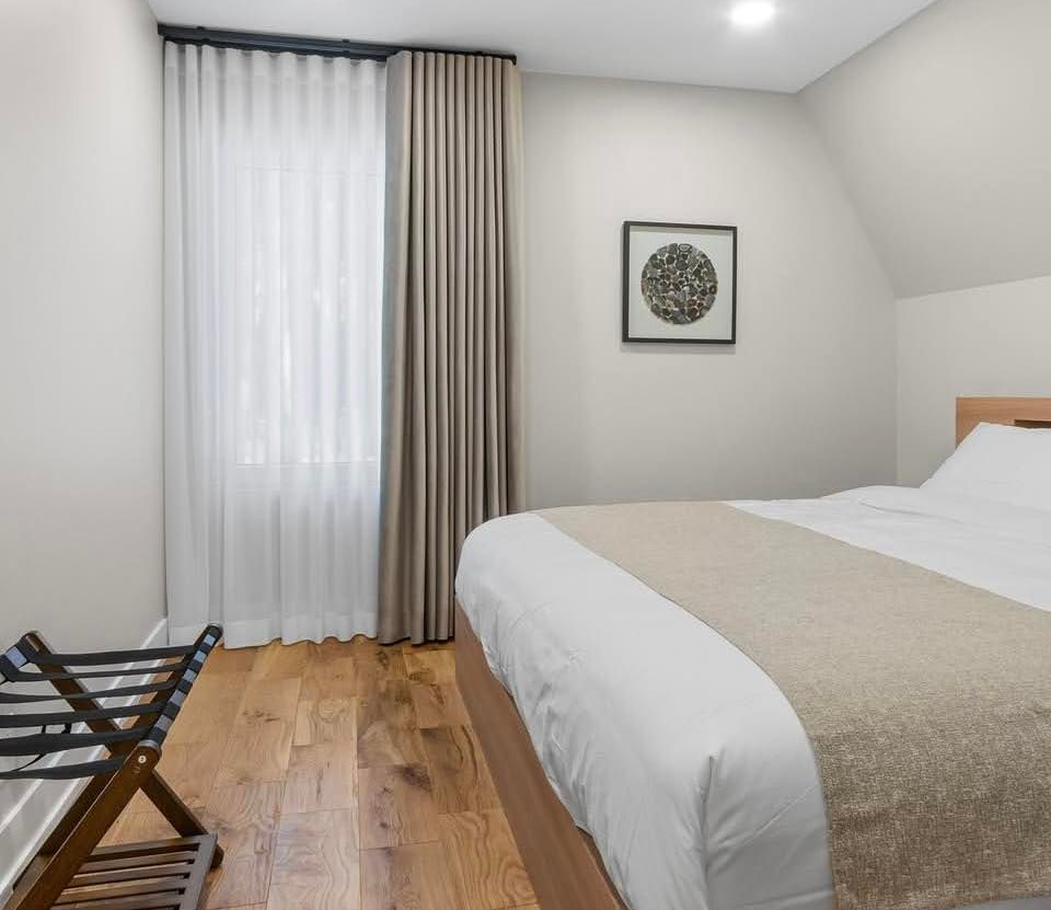Minimal bedroom with bed, wood floor, curtains, wall art, and luggage rack.