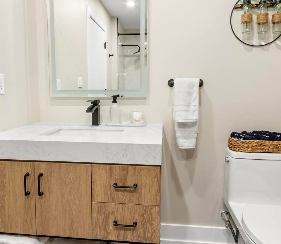 Modern bathroom vanity with white sink, wood drawers, mirror, towel rack, and toilet in a bright room