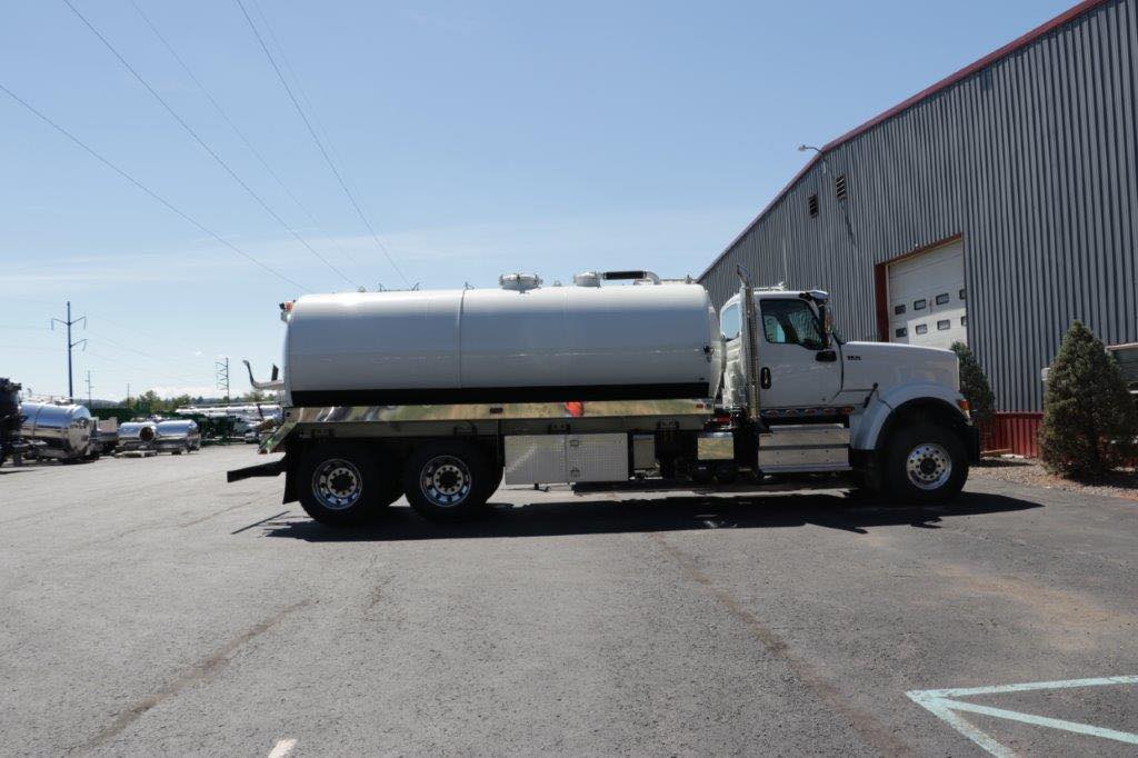 A white tanker truck is parked in front of a building.