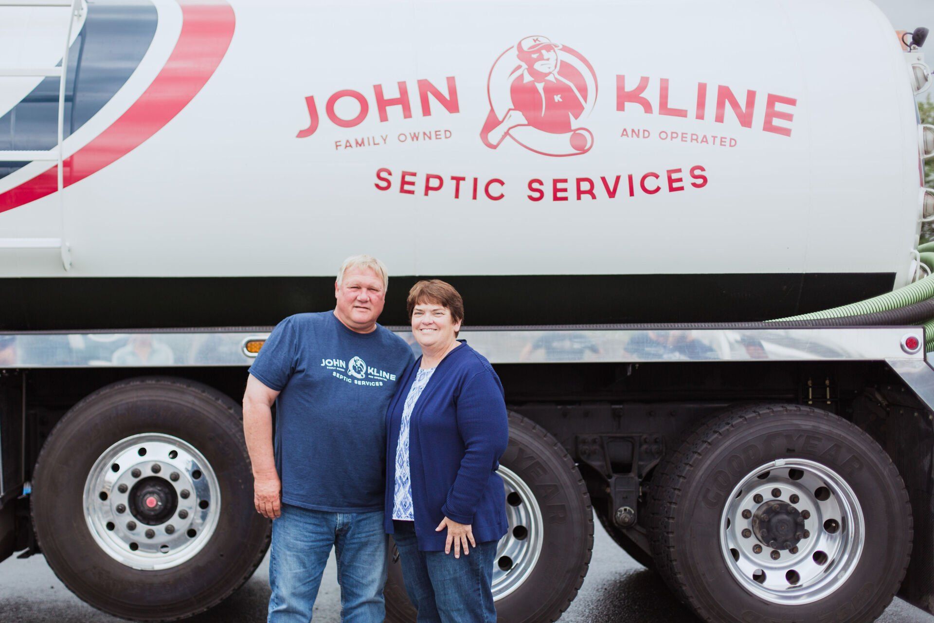 A man and a woman are standing in front of a septic service truck.