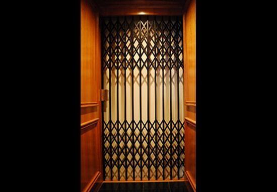 A black scissor-style metal elevator gate between dark wood paneled walls.