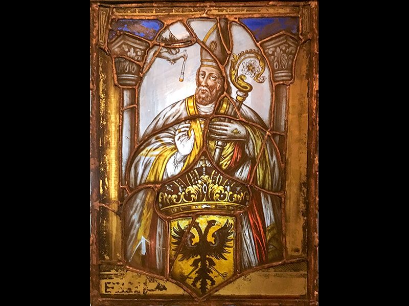 Stained glass of a bishop holding a crozier above a yellow shield with a black double-headed eagle emblem.