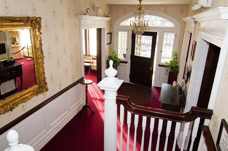 An interior view from a staircase looking down at an entryway with a red carpet, dark wooden door, and crystal chandelier.