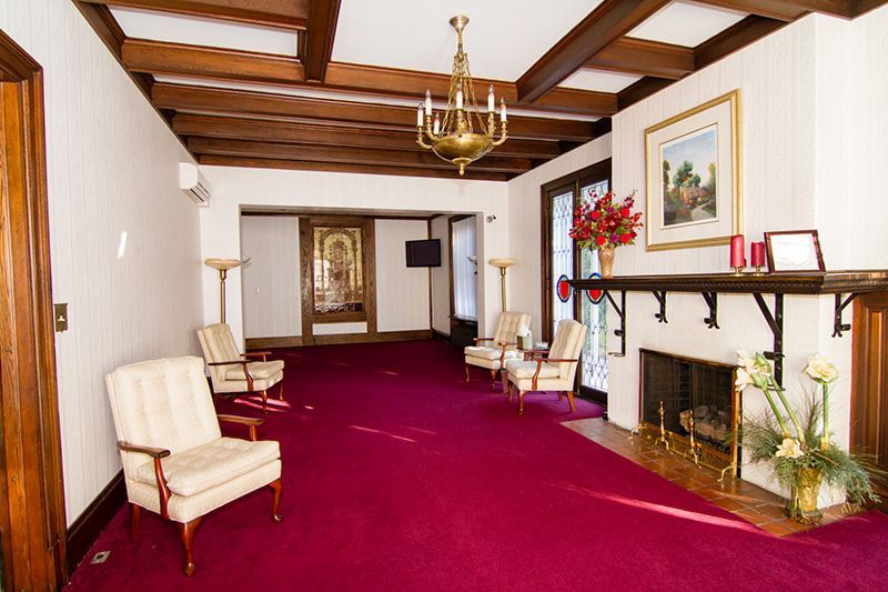 A formal living room with cream chairs, red carpeting, a chandelier, and a fireplace with a mantel.