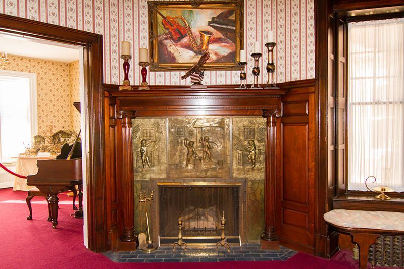 A wooden fireplace mantel with ornate gold-tone metal panels, topped by a painting and candles in a Victorian room.