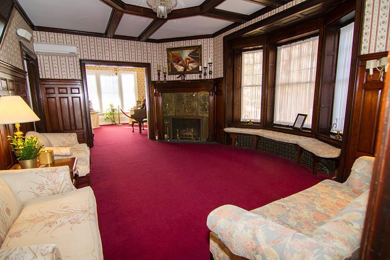 A spacious room with red carpet, wood-paneled walls, a fireplace, and patterned upholstered furniture.