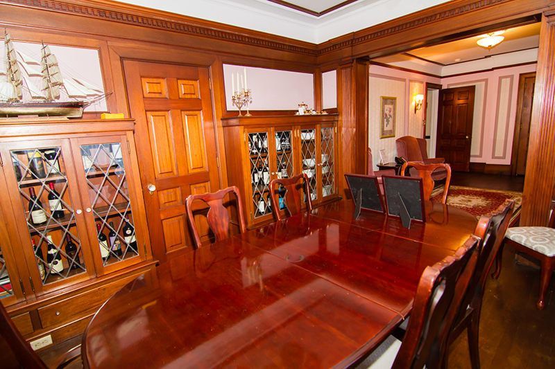 Formal dining room with dark wood paneling, a glossy table, and a glass-front display cabinet containing bottles.