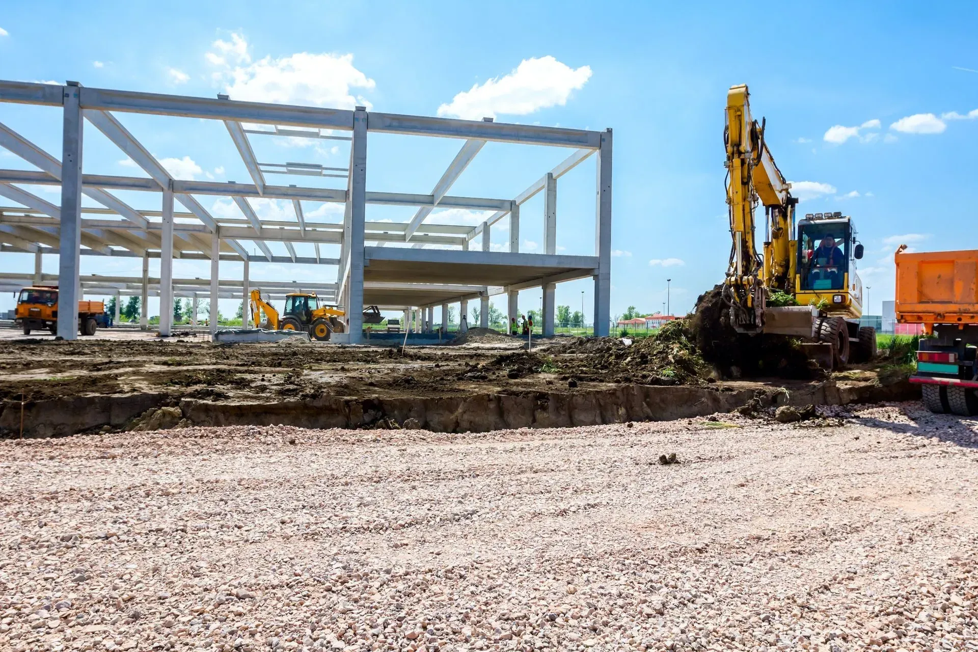 Construction site with steel frame building and yellow excavator under blue sky