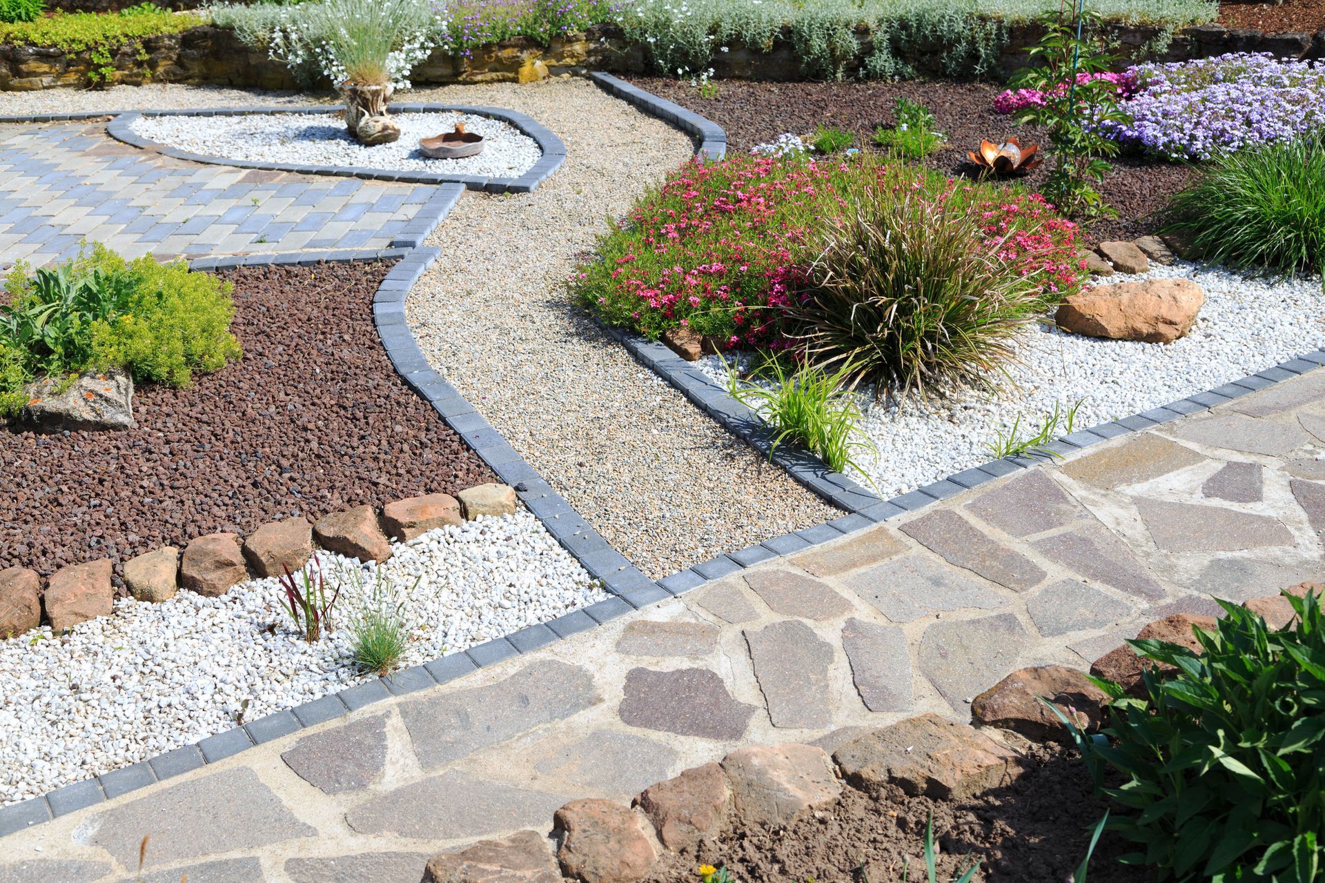 A stone walkway in a garden surrounded by rocks and flowers.