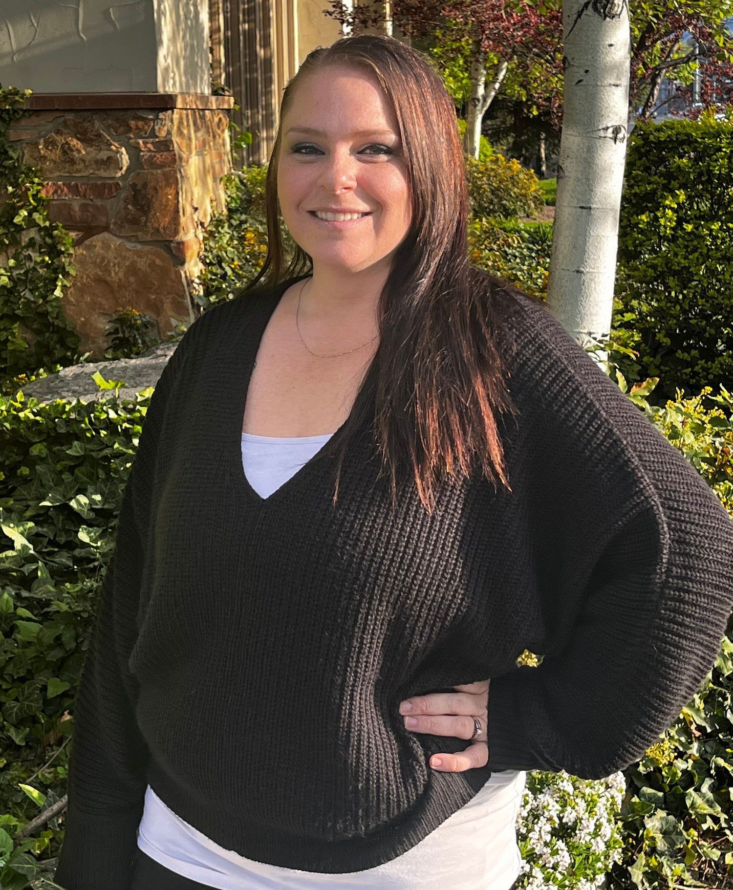 A woman in a black sweater is standing in front of a tree.