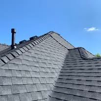 Dark gray shingle roof on a house against a bright blue sky, chimney in view.