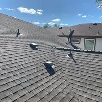 Dark shingle roof with vents, a wind-powered turbine, and a blue sky background.